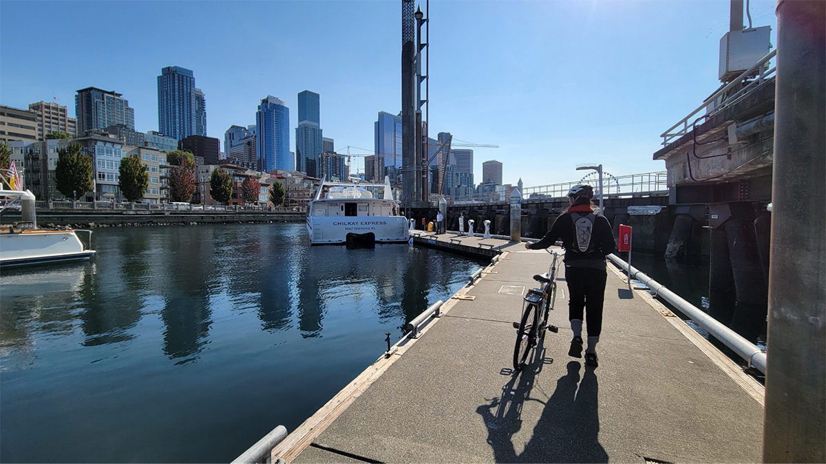 A woman walks her bike down a floating dock.