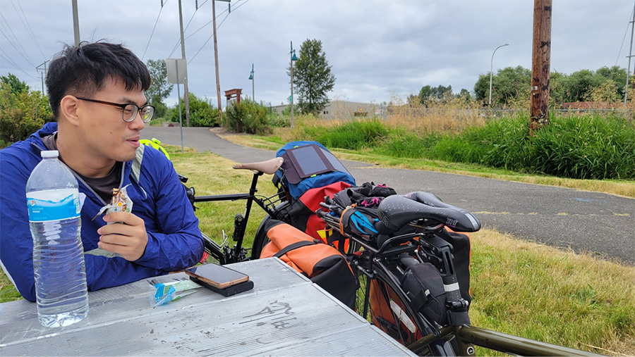 A man eats at a picnic table next to his loaded bike.