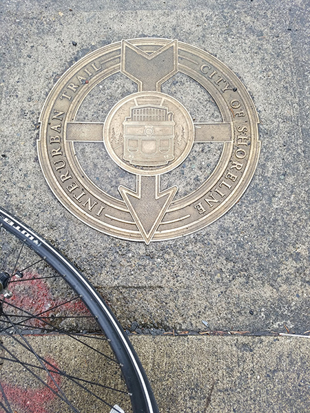 Metal marker in concrete that reads "City of Shoreline. Interurban Trail." With an engraved trolley.