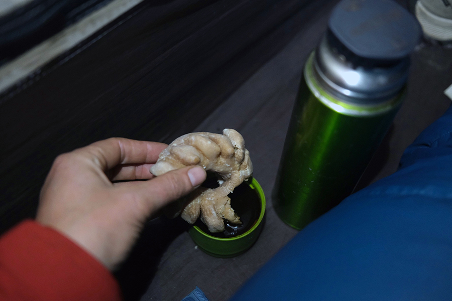 A hand hold a donut that has been dipped into the cup of a thermos.