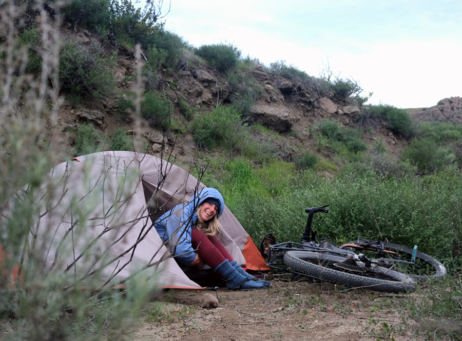 Laura leans out from her tent smiling with her bike lying nearby.