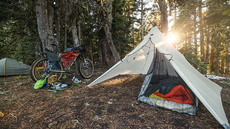 A pyramid tent with sleeping bag inside, next to a loaded bike in a forest.