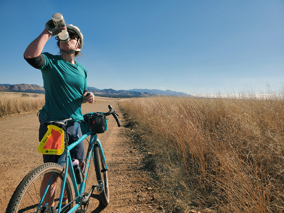 A cyclist chugs her water bottle in a dry grassy area.