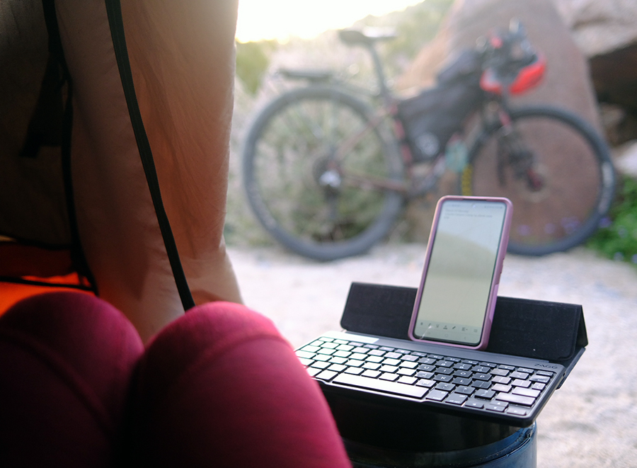 A phone sits on a portable keyboard in a tent. Outside a bicycle is in view.