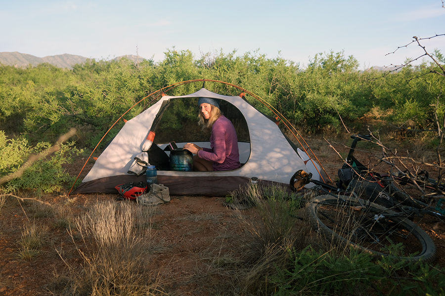 A woman types in her tent with the rainfly off.