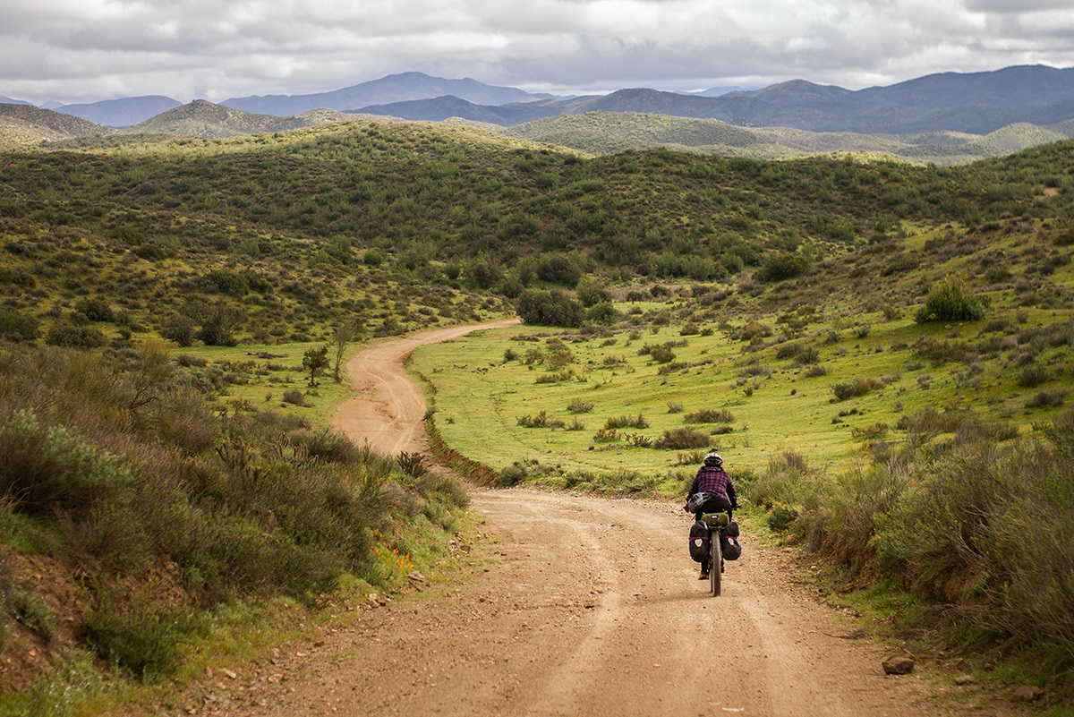 Karla rides away from the camera along a dirt road in rural Mexico