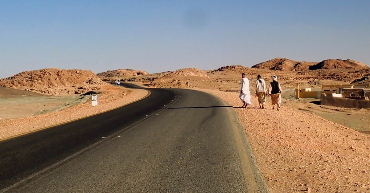 Sudanese men walk along a desert road