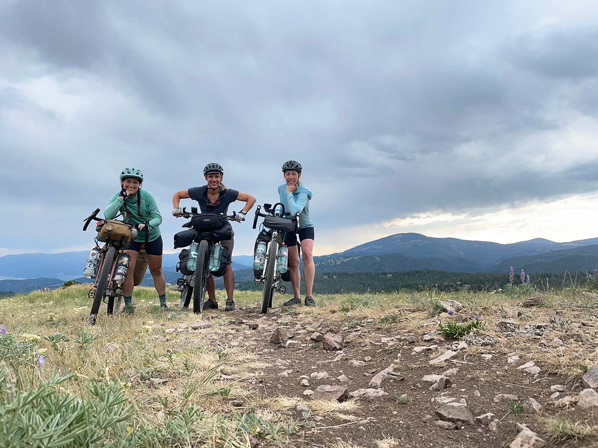 Three white, young-ish women stand on a scenic overlook with their fully loaded bike rigs.