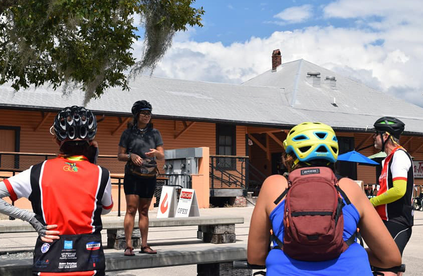 Ana stands on a picnic table and has a pre-trip meeting with participants.