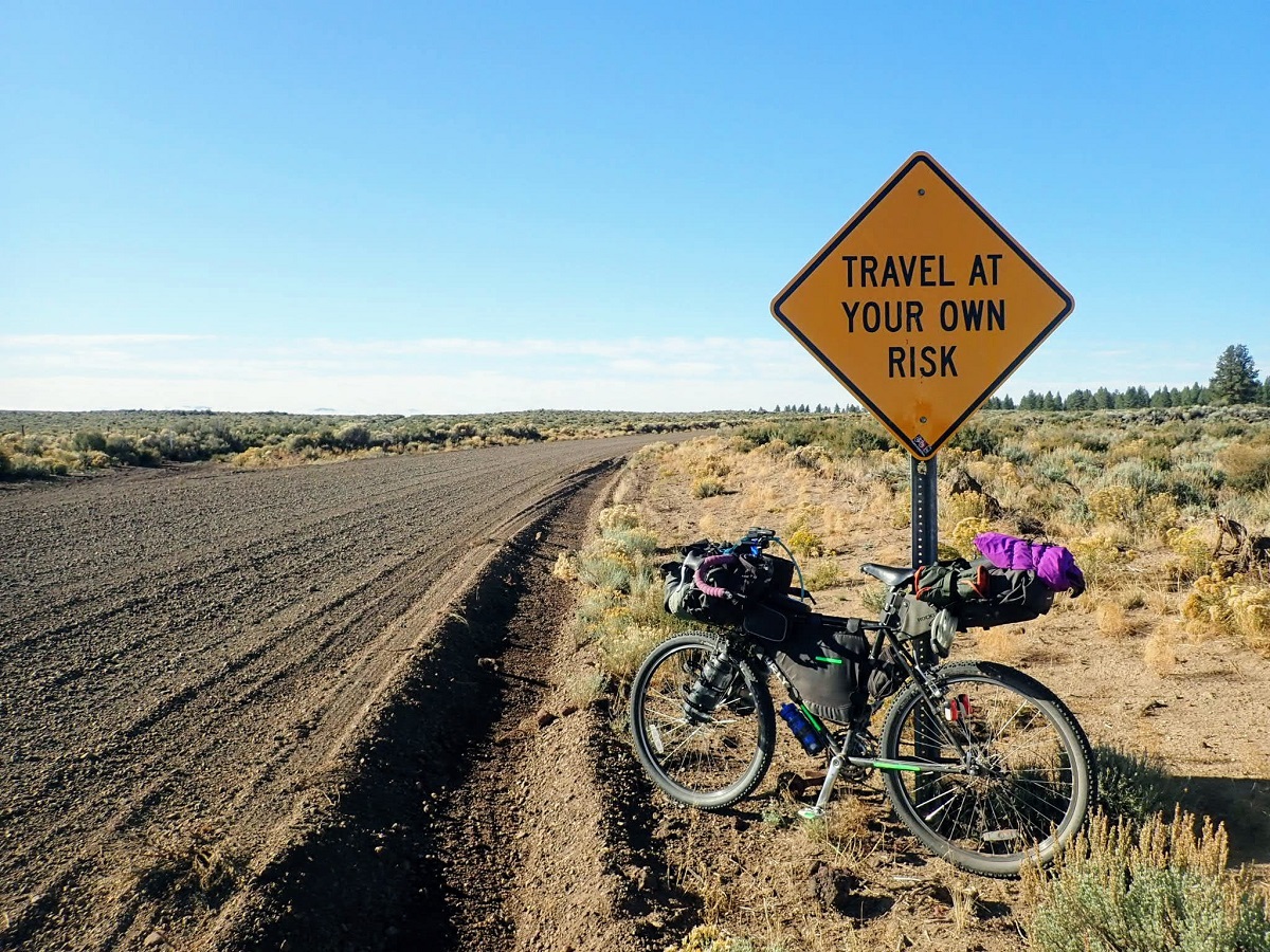 Bicycle against road sign that says Travel at Your Own Risk