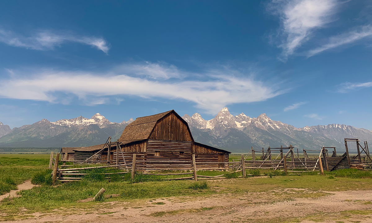 An incredible view of a big old barn against a mountain and blue sky backdrop