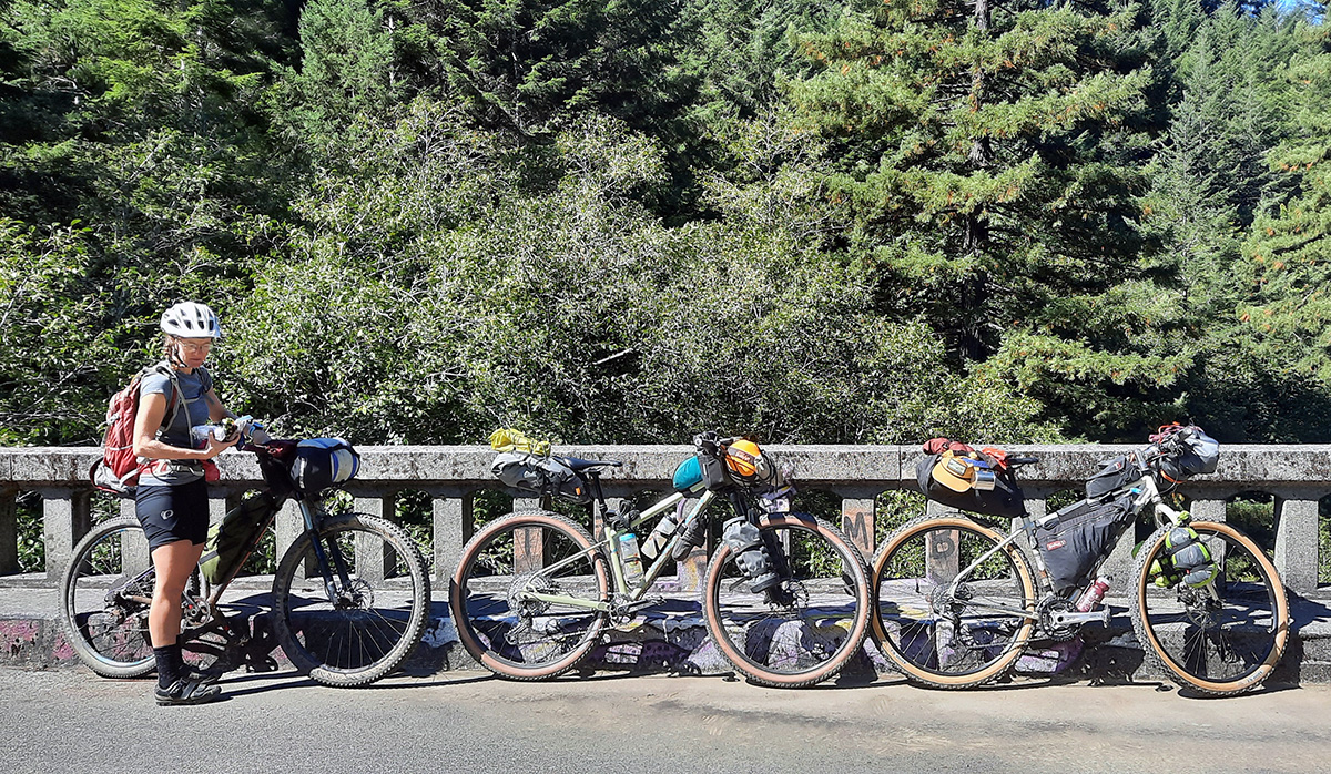 Pictured are three bikes leaning against a bridge railing and Hollie who is holding her burrito wrapped in foil.