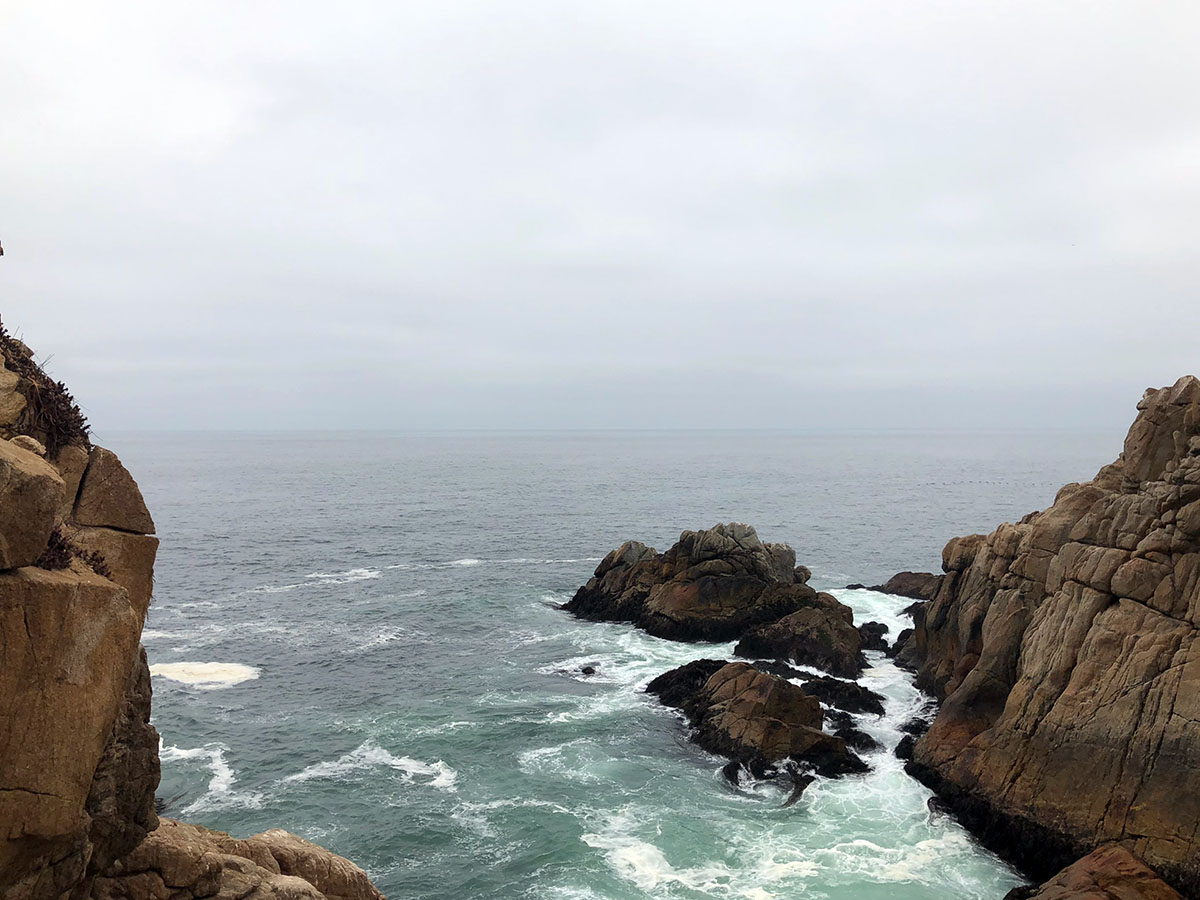 Brown cliffs and a gray sea with big waves crashing against the rocky land. 