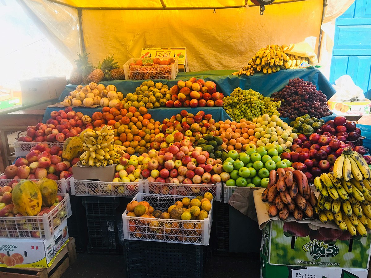 A large fruit staff is full of many varieties of mangos, grapes, pineapples, bananas, apples, and melons, all sitting under a yellow tent.