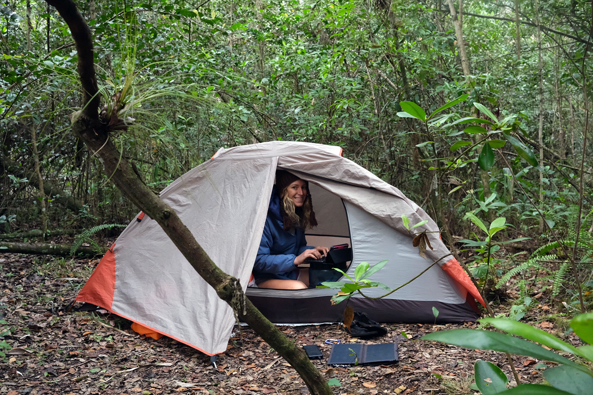 Laura peeks out of her tent's open door as she writes a story on a small device while in the middle of the Florida jungle.