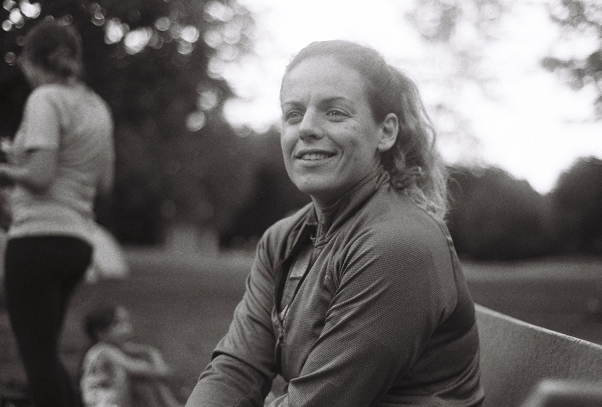 Marina sits around the fire and smiles into the camera in this grainy black and white film photograph