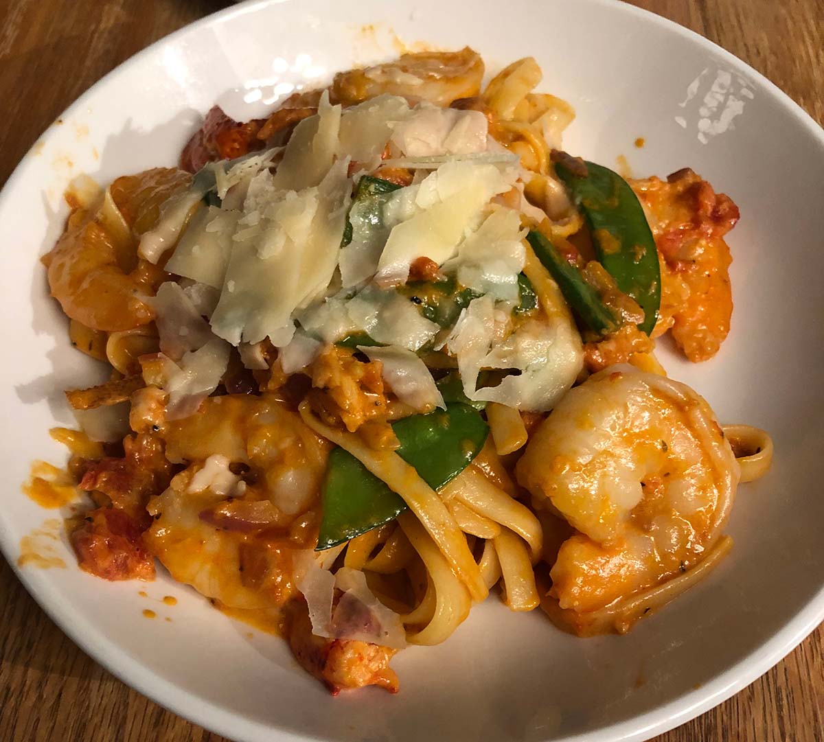 A plate of thick ribboned pasta with a light red sauce, pink shrimp, and rustic grated cheese.