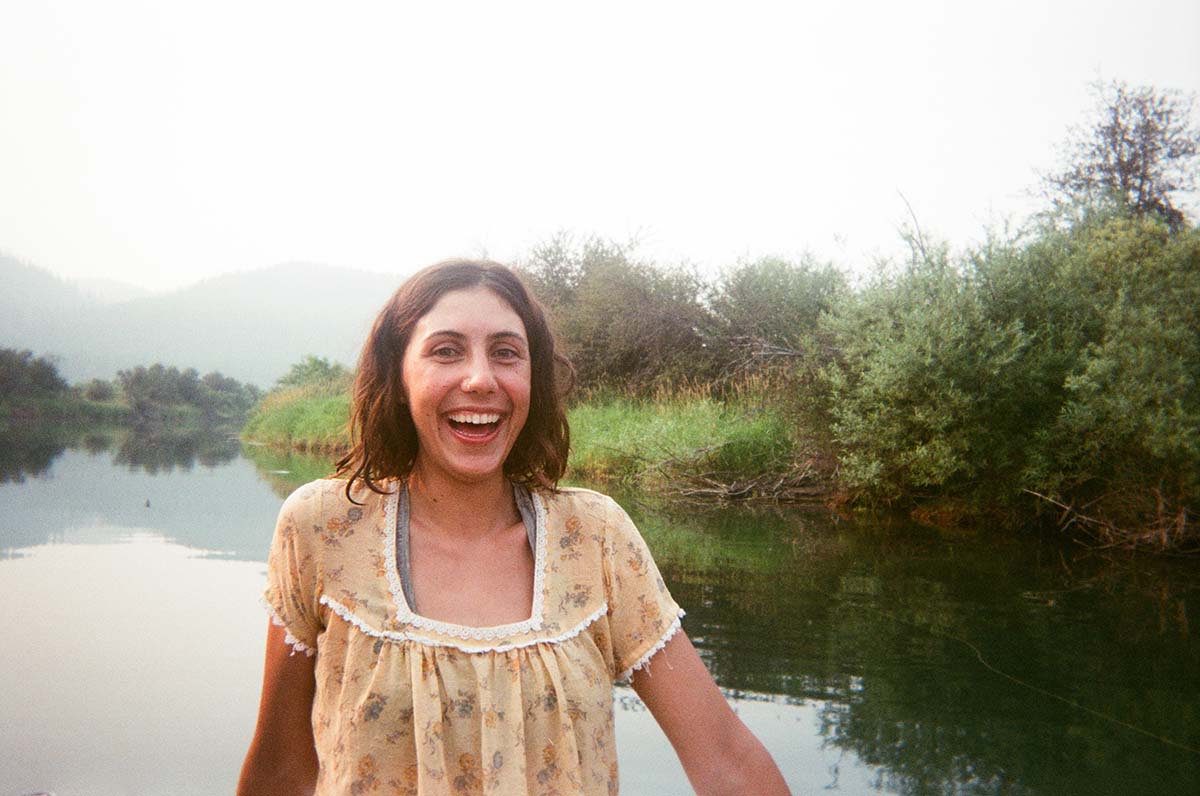 Mia, a young white woman, sits on a boat wearing a yellow dress with tiny flowers on it.