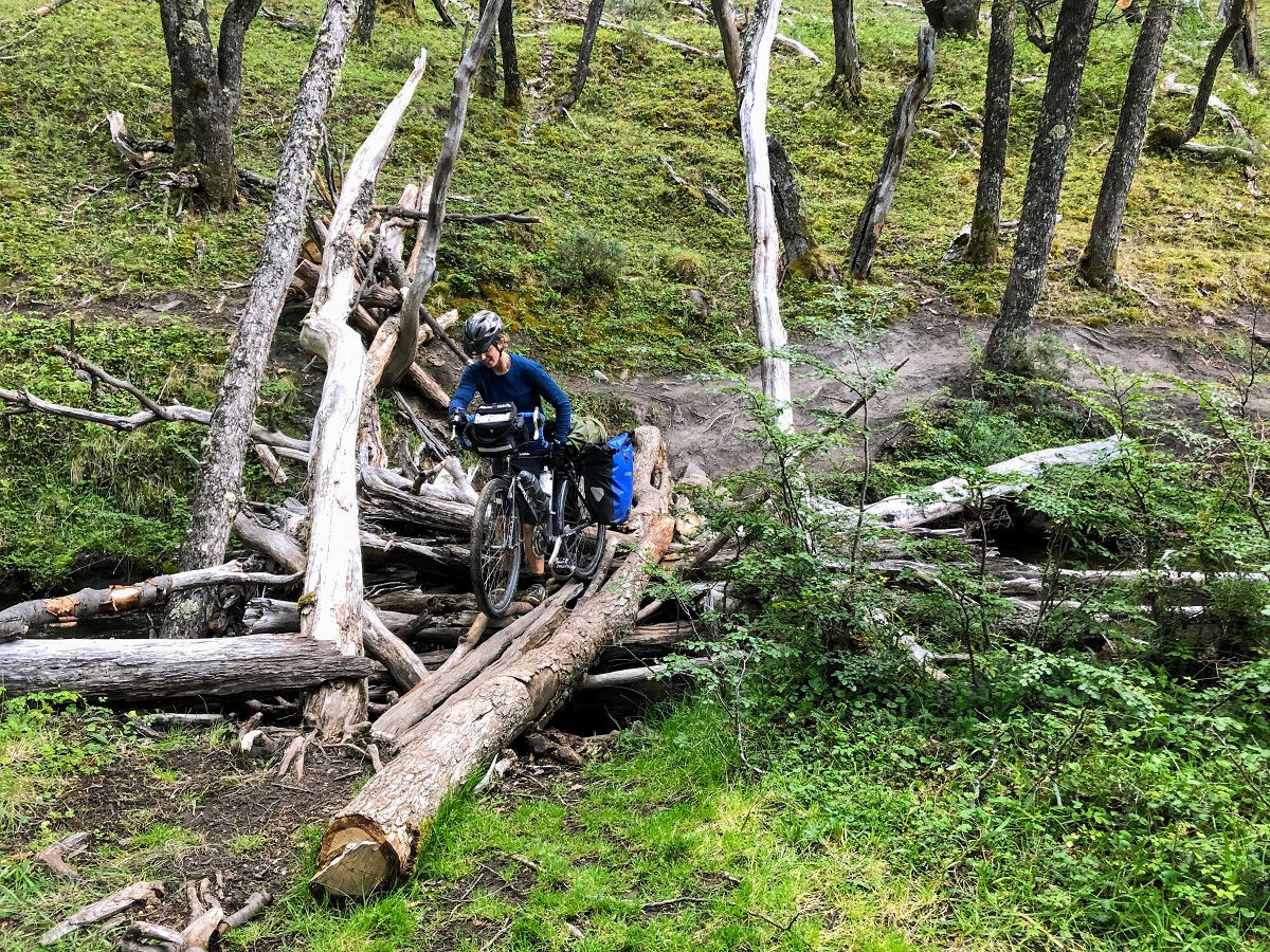 Alissa walks her loaded bicycle across some logs while bikepacking in Chile.