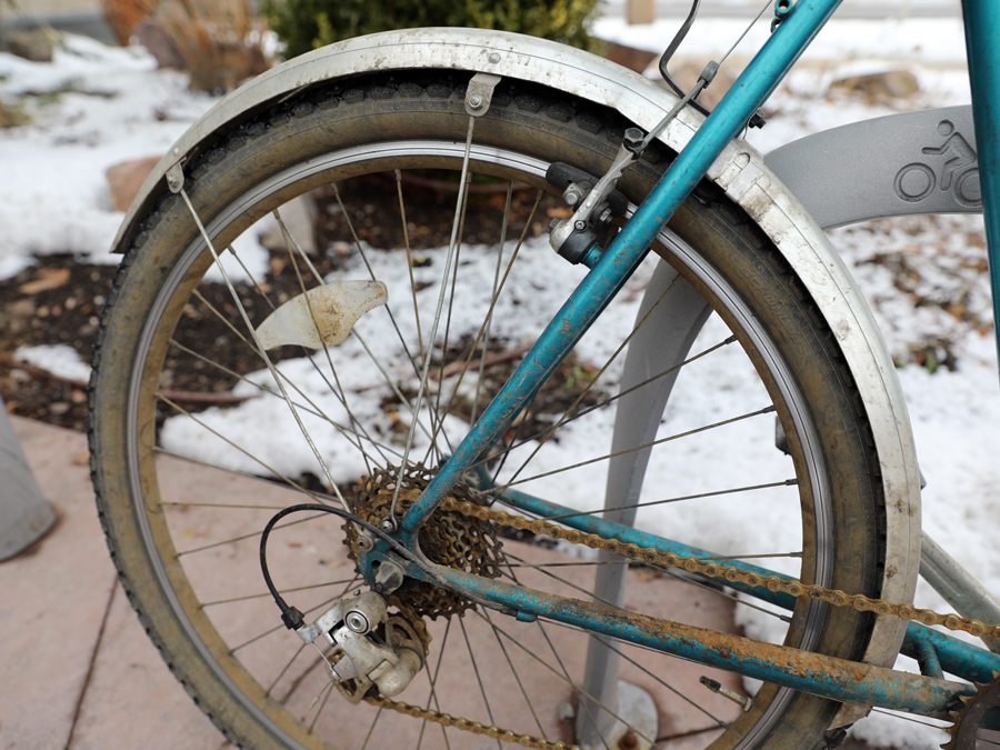 A full-length metal fender on a bike with a rusted chain