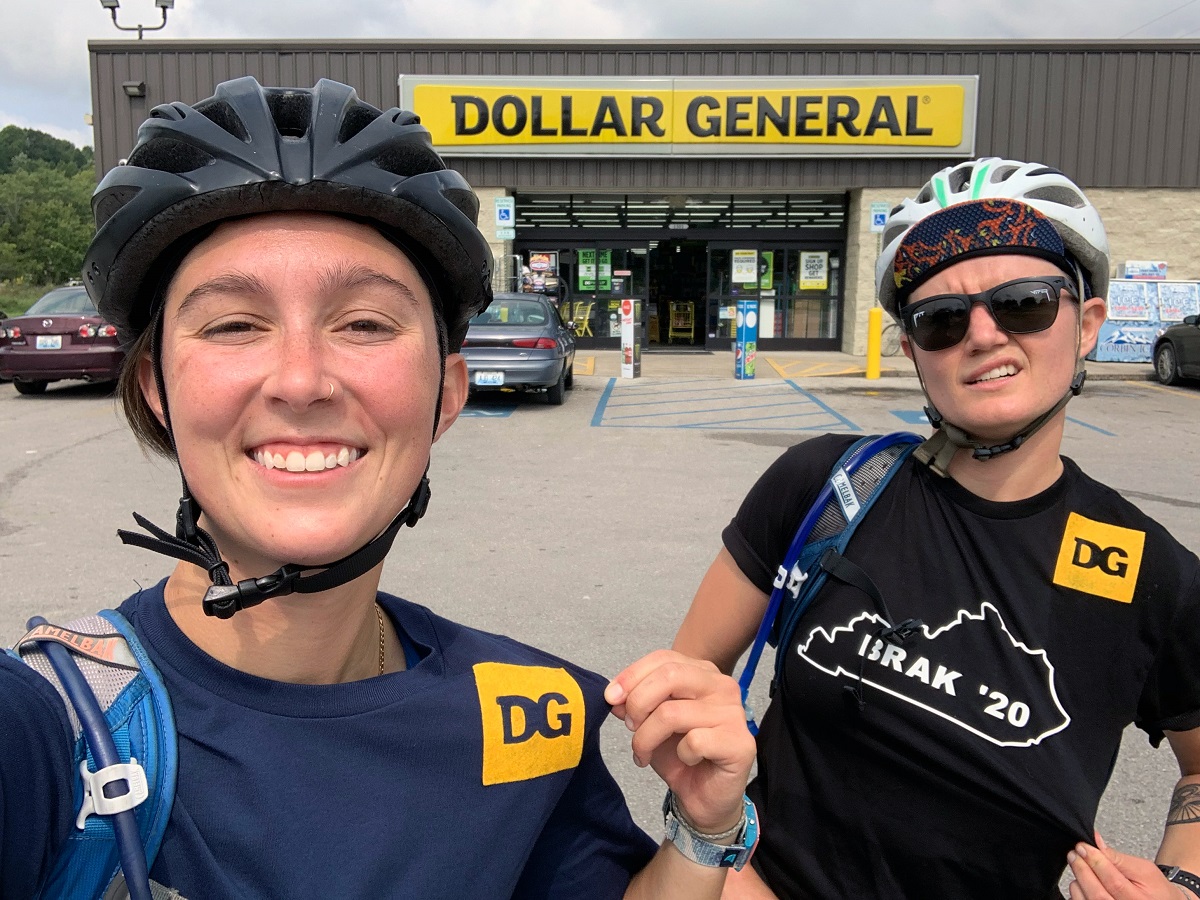 Sydney and Amanda add DG to their "cycling kits" aka their tshirts as they stand in front of a Dollar General store.