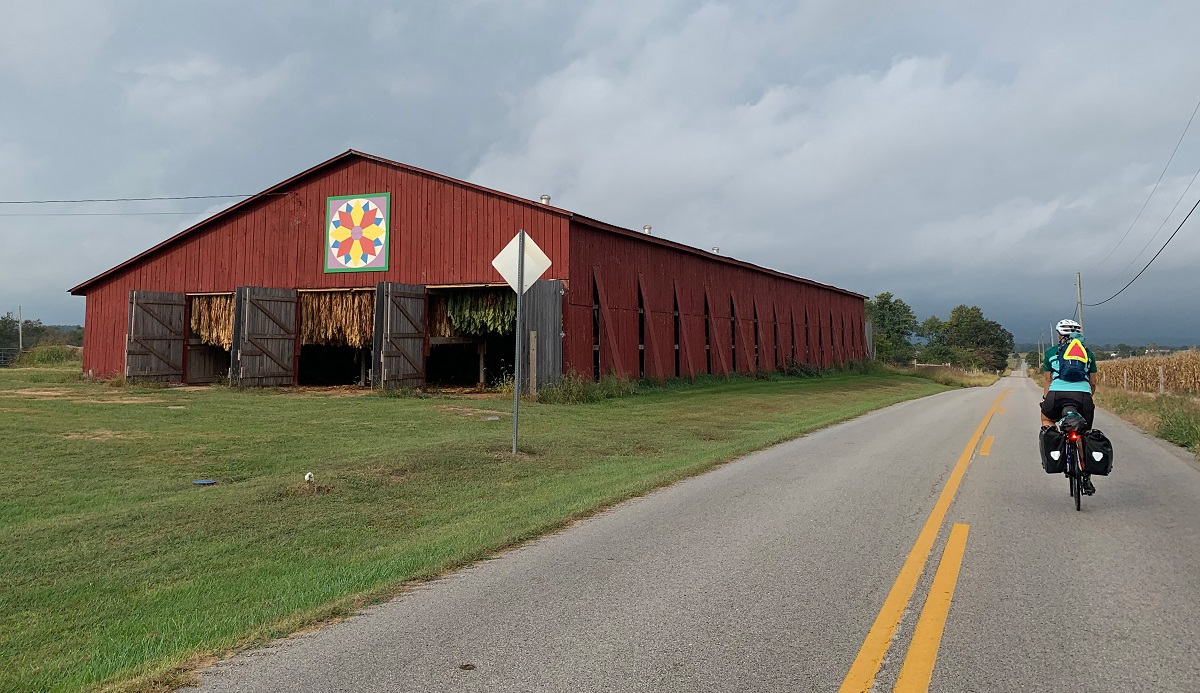 Syd's friend and riding partner, Amanda, cycles past an old Kentucky barn with a storm looming in the distance.