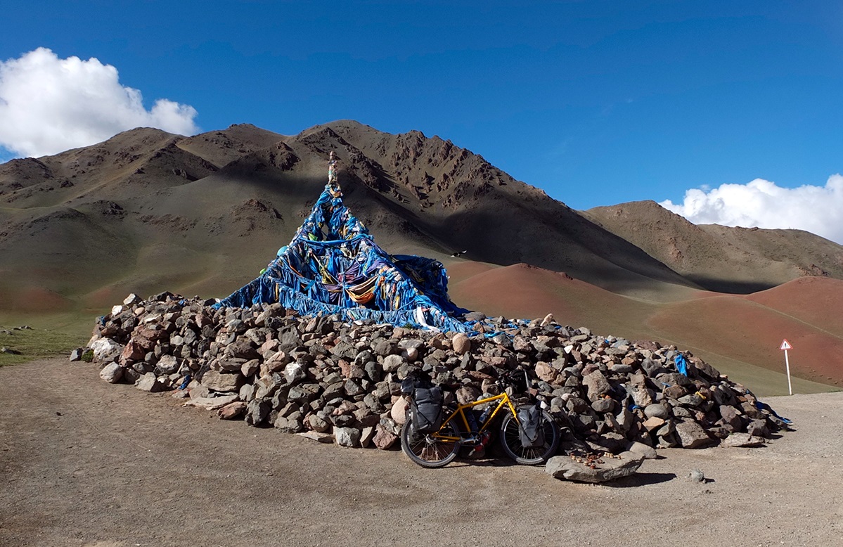 At the top of a mountain pass is a pile of rocks with a pole covered in colorful silk strands