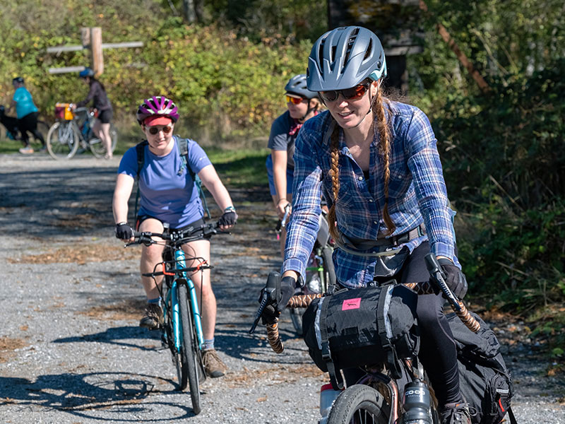 Three cyclists riding on gravel. The one in front looks like she's focusing on the terrain ahead.