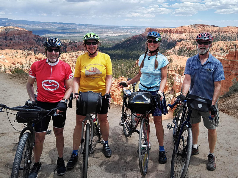 Four smiling cyclists standing with beautiful canyon in background.