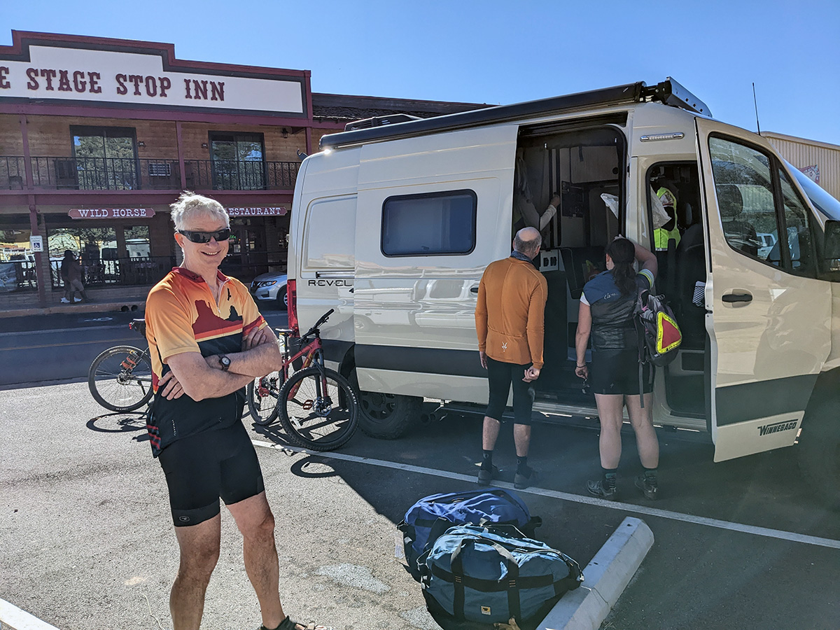 A cyclist smiling with arms folded. Two cyclists peer into a van in front of the Stage Stop Inn.