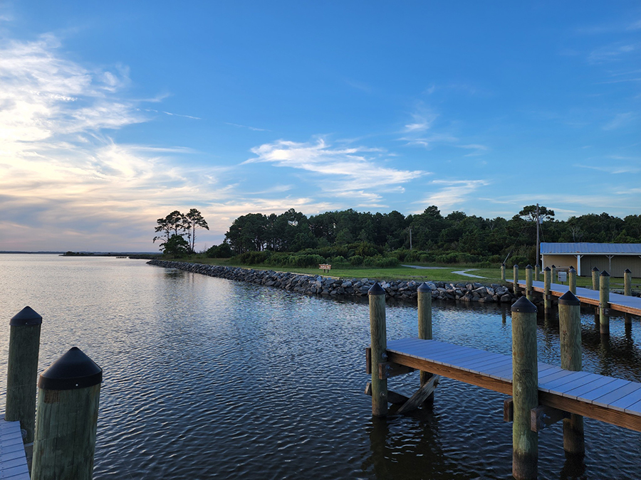 A dock on calm water with a view of trails and a forest.