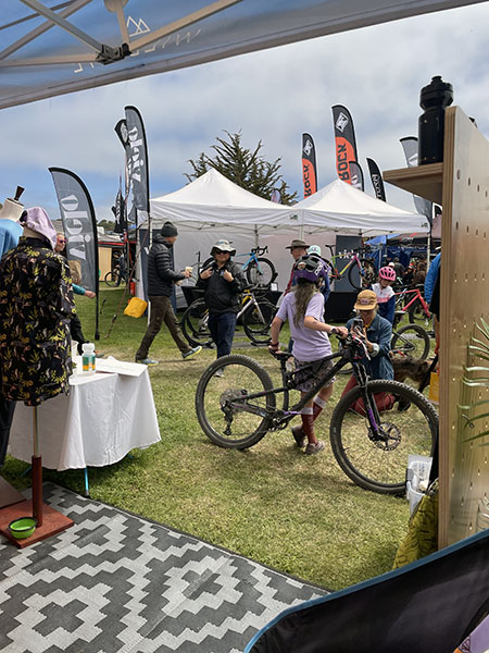seen from the inside of a booth: a woman in purple leans on her bike