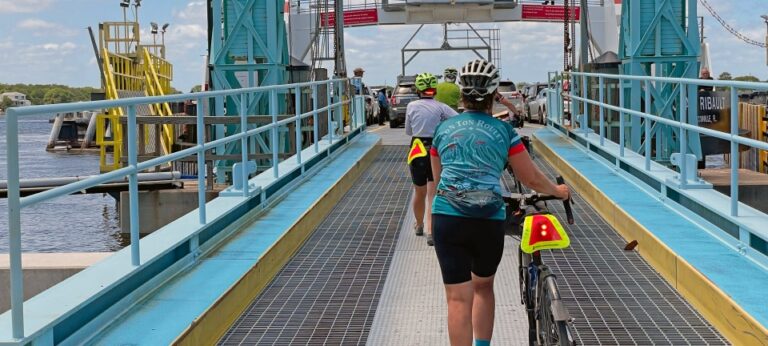 Cyclists enter a river crossing boat in Florida, walking with their bicycles to the main boat platform