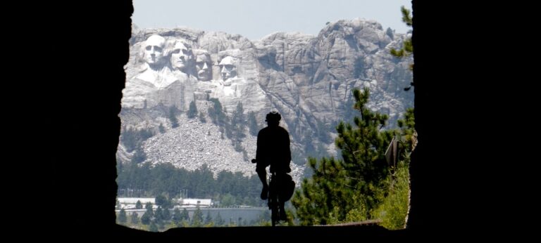 A cyclist rides through a tunnel, revealing a magnificent view of Mt Rushmore