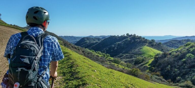 A male cyclist gazes out over a lush, rolling green field while stopped on his bike